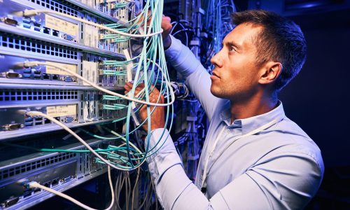 Serious concentrated data center IT technician checking network cables connected to server